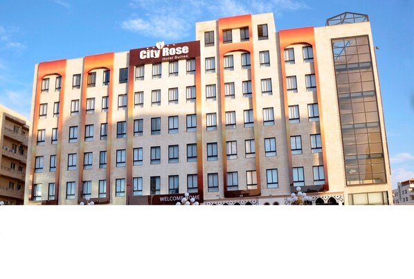 Un hotel de varios pisos con un diseño moderno, que presenta un llamativo letrero que dice 'City Rose Hotel Suites'.