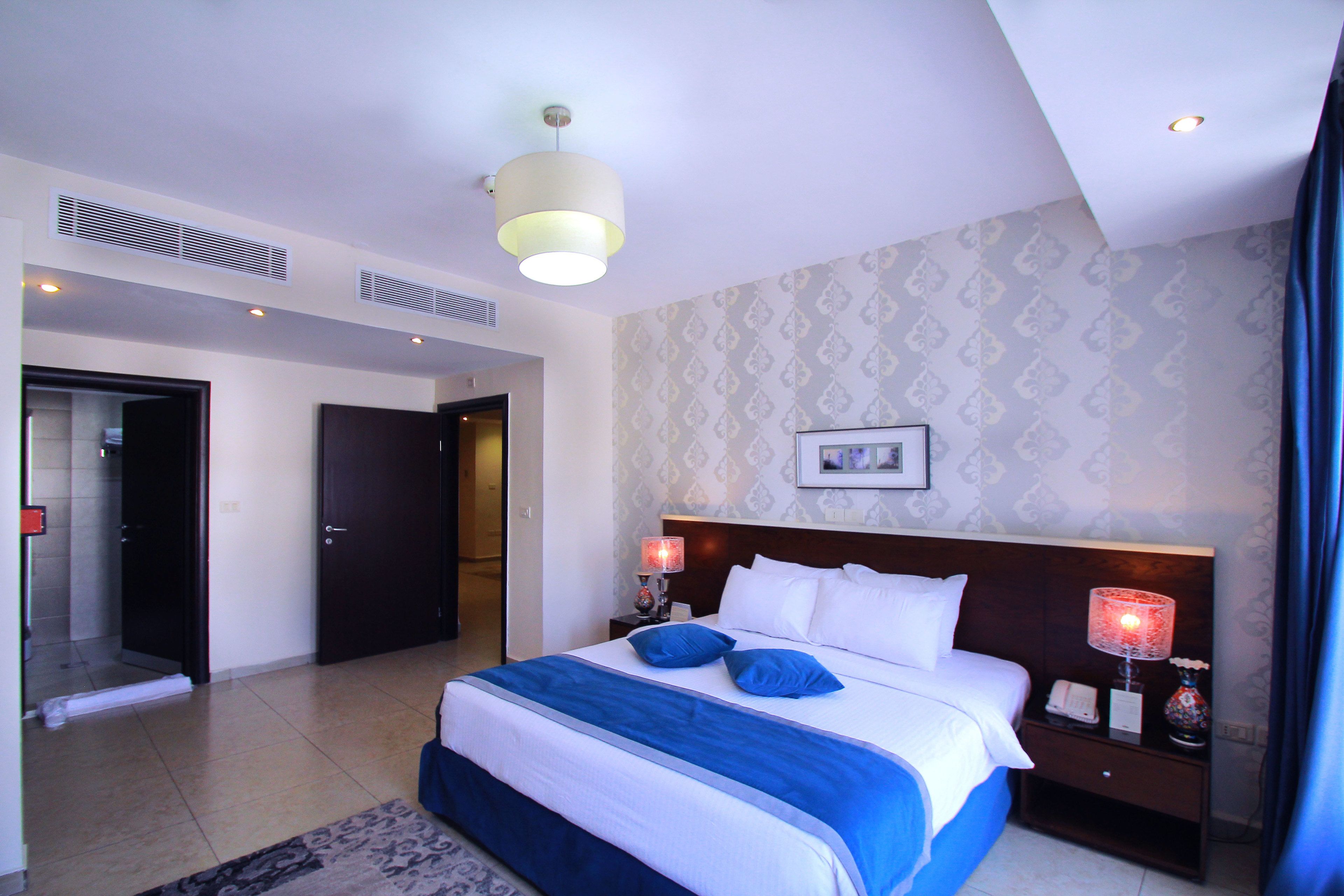 A hotel room with a large bed, two bedside lamps, a nightstand, a headboard, and a ceiling light.