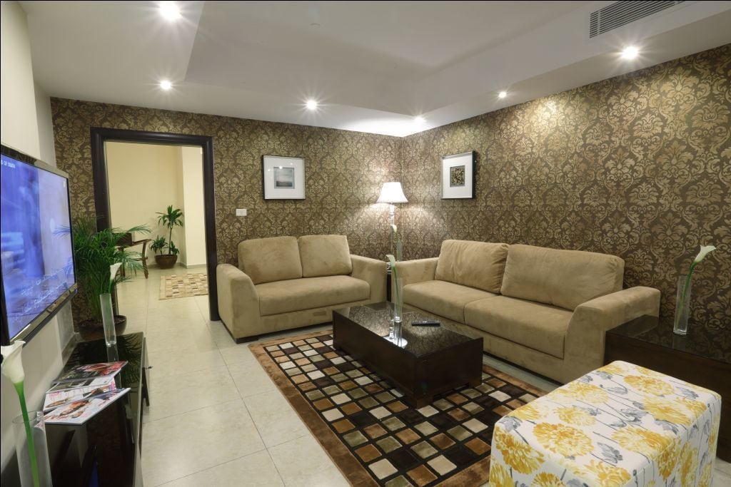 A living room with two beige sofas, a coffee table, a TV, and a patterned wall.