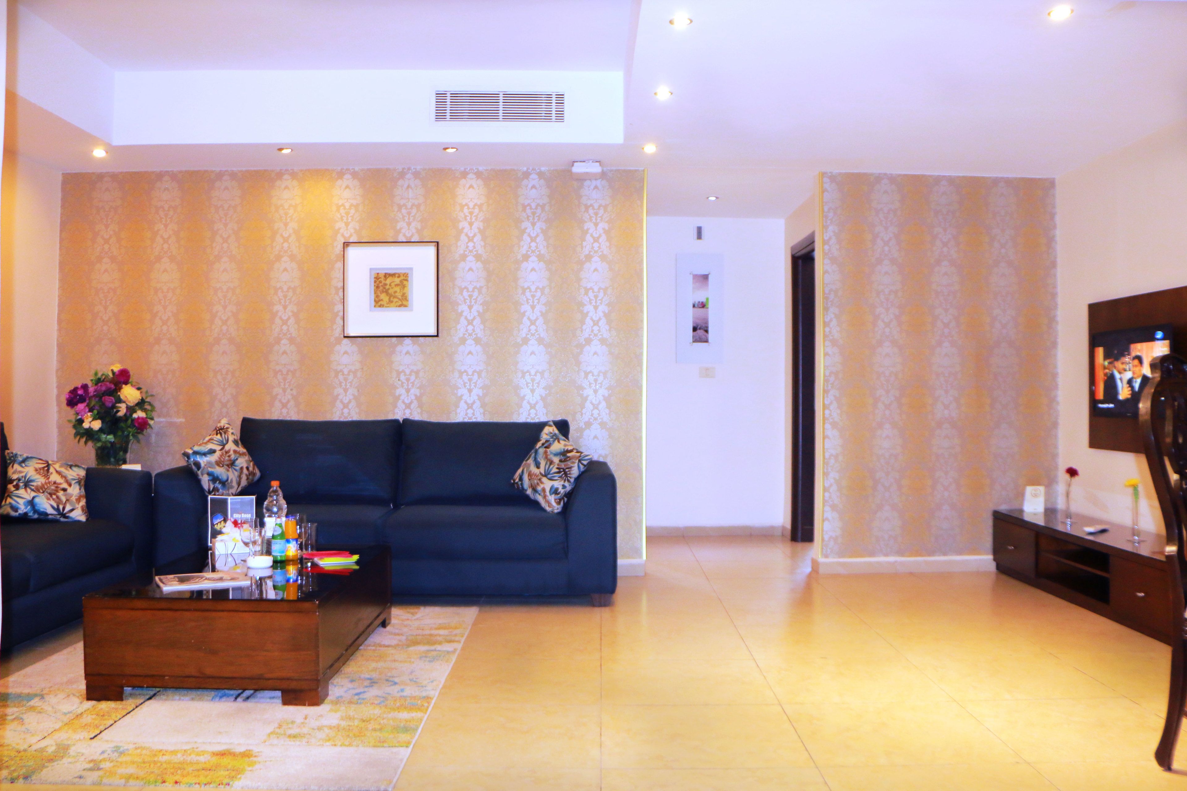 A living room with a dark blue sofa, a coffee table with various items, and patterned wallpaper.