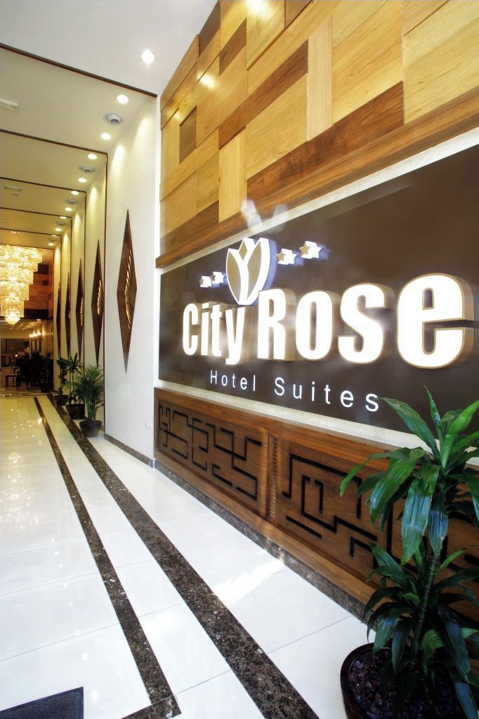 A hotel entrance with a sign reading "City Rose Hotel Suites" and a modern interior design.