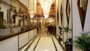 A hotel corridor with a chandelier, potted plants, and a reception area with glass display cases. - City Rose Hotel Suites (Amman)