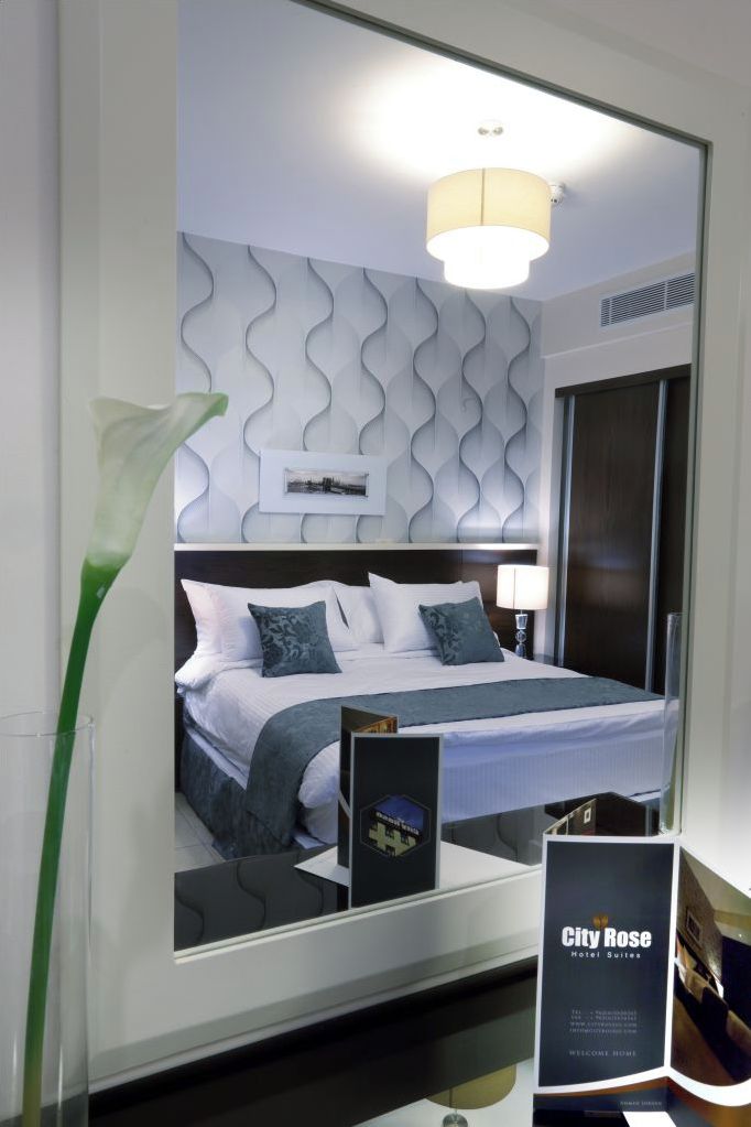 A modern hotel room with a large bed, a decorative wall, a nightstand, and a mirror.