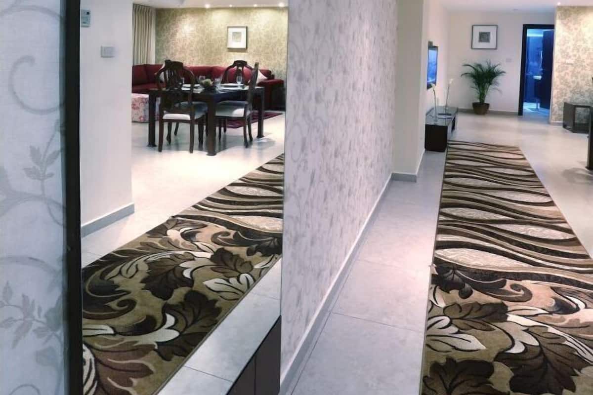 A modern hotel lobby with a long mirror, a patterned carpet, and a dining area in the background.