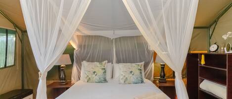 A four-poster canopy bed with white linens, two nightstands with lamps, and a bedside table with a clock and a bottle.