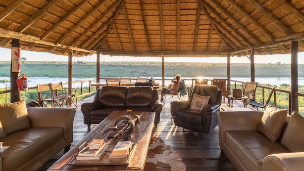 A covered outdoor seating area with leather sofas and a wooden coffee table, overlooking a body of water.