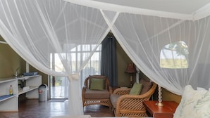 A room with a canopy bed, wicker furniture, a small table, a lamp, and a view of the outdoors.