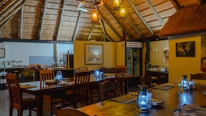 A restaurant with wooden tables and chairs, lantern-style lighting, and a thatched roof.