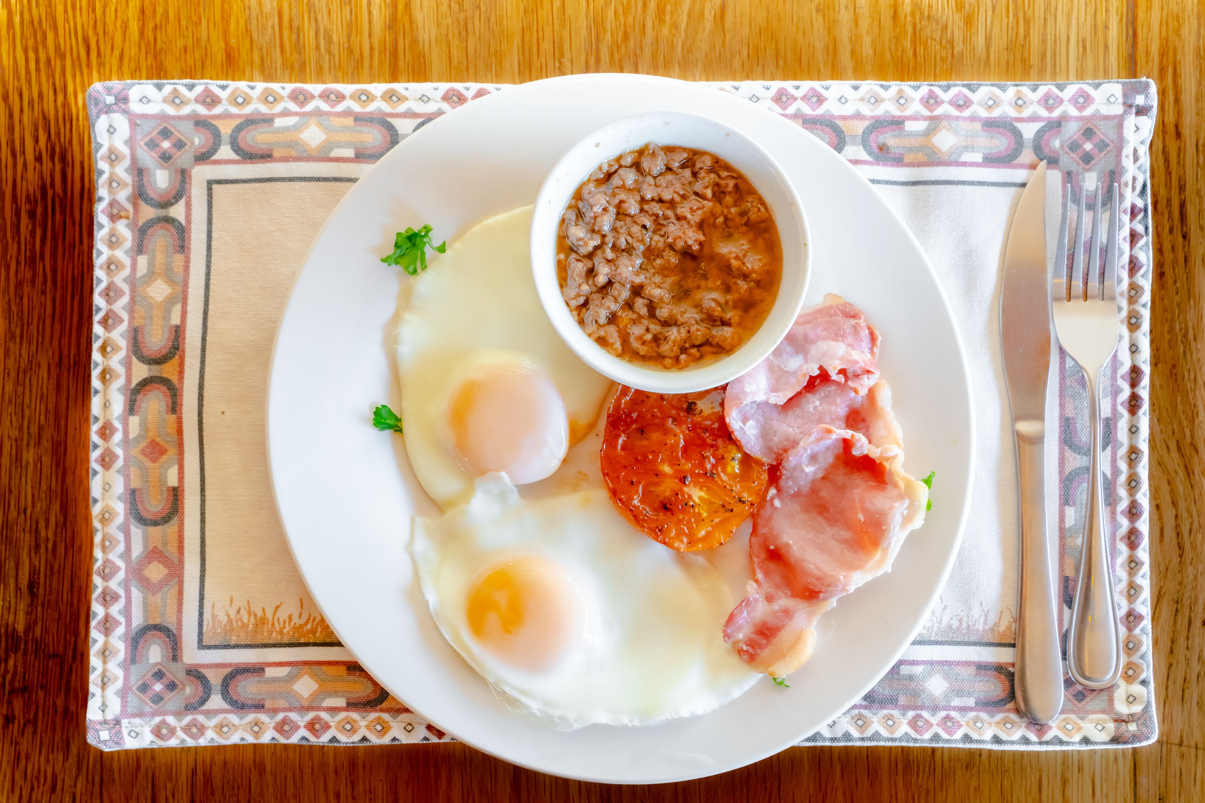 A plate with eggs, bacon, and beans on a patterned placemat.