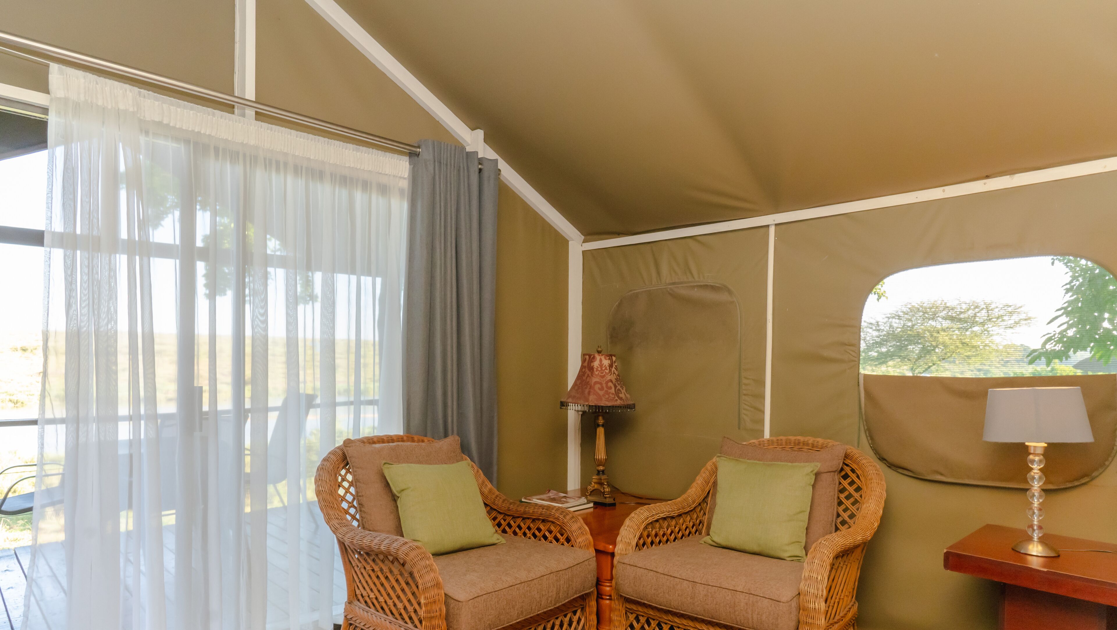 A tented room with two wicker chairs, a table, and a lamp.