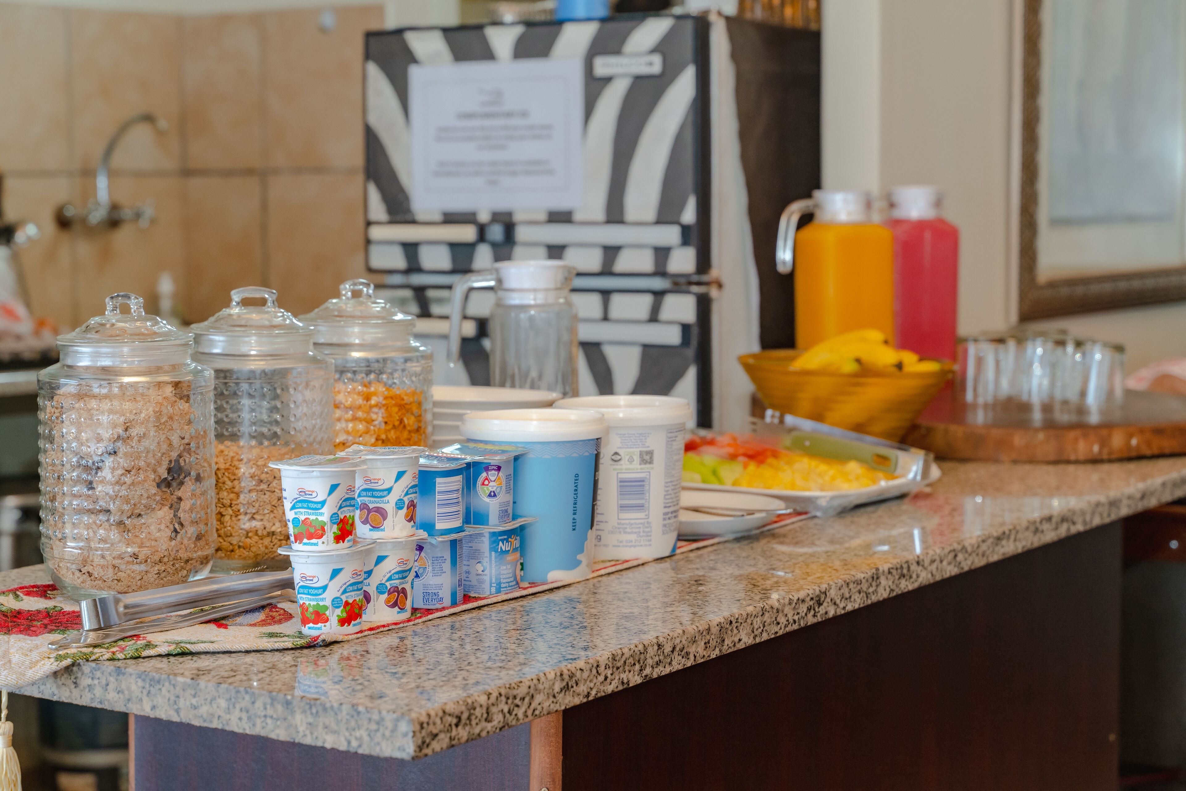 A breakfast bar with various food items and beverages, including cereal, yogurt, and juice.