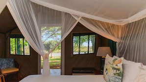 A bedroom with a canopy bed, two windows, a chair, and a bedside table with a lamp.