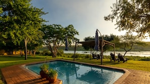 A rectangular swimming pool with a brick border, surrounded by a grassy area and trees.