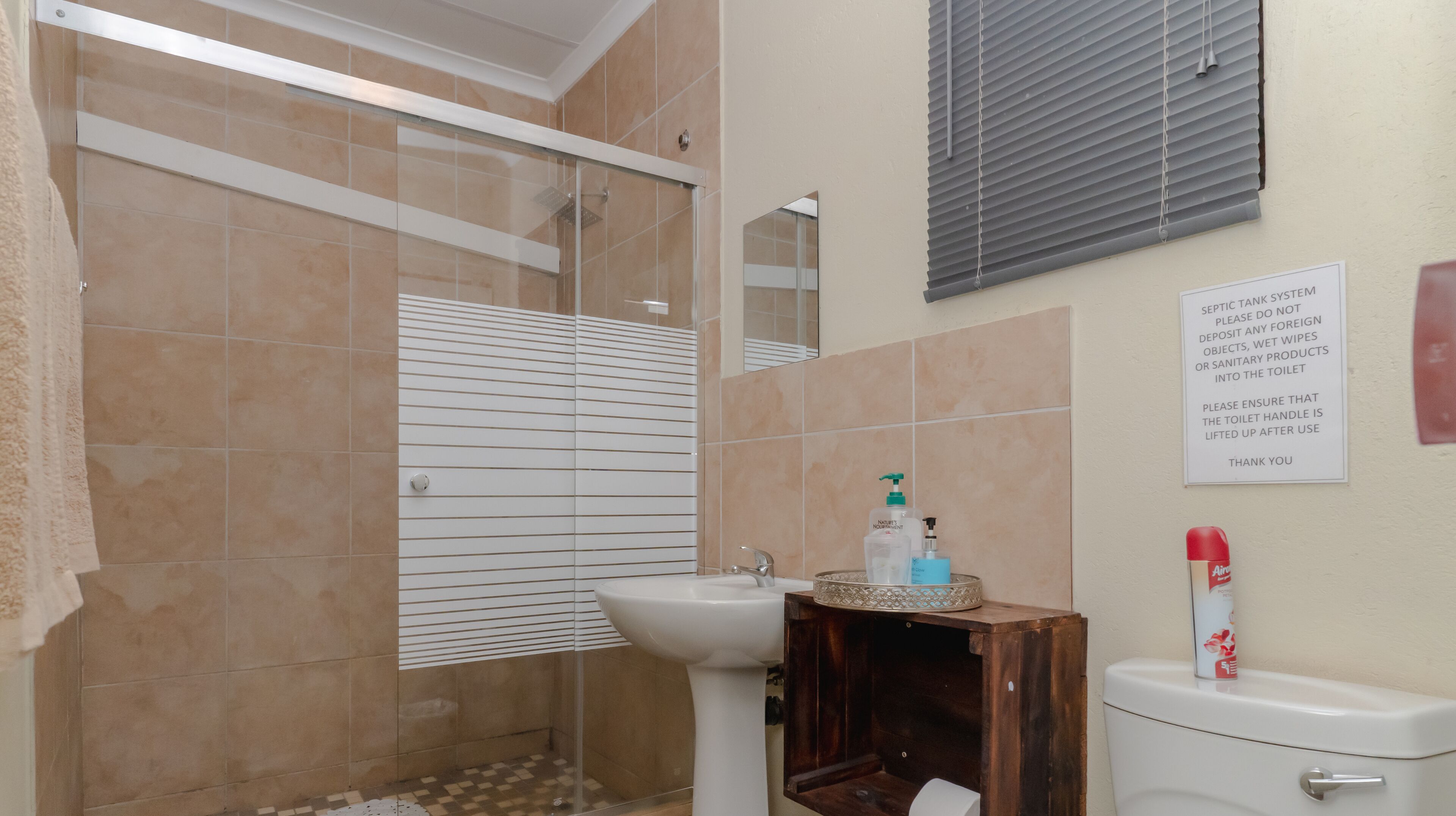A bathroom with a shower, sink, and toilet. There is a sign on the wall with instructions for the septic tank system.
