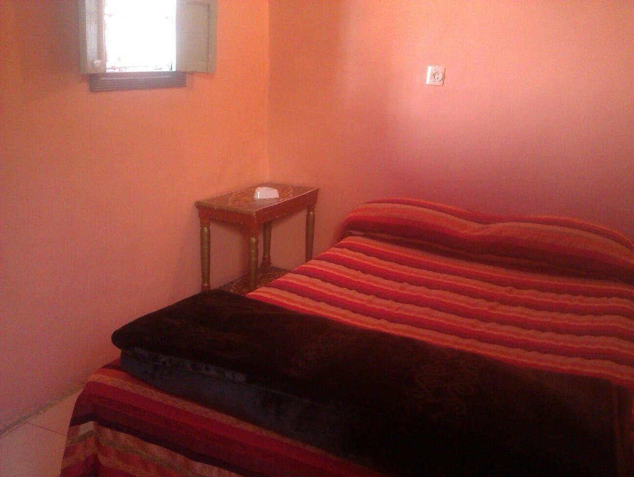 A small bedroom with a bed, a nightstand, and a window.