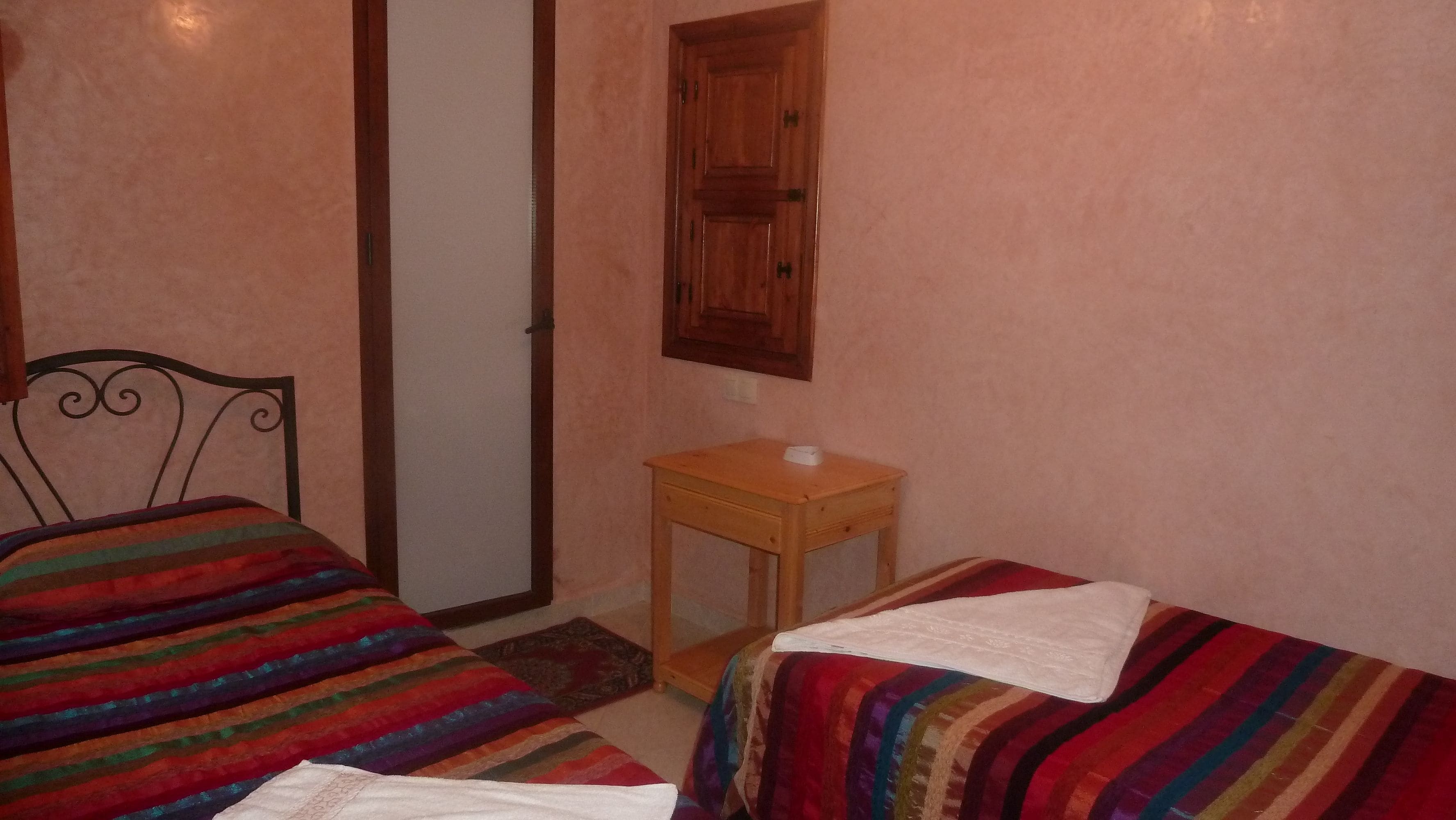 A bedroom with two beds, a wooden nightstand, and a door.