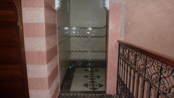 A hallway with pink walls, a tiled floor with geometric patterns, and a metal railing.