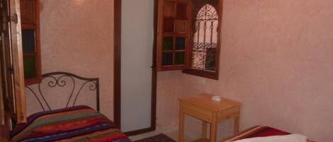 Un dormitorio con una cama, una mesita de noche de madera, una ventana con rejas decorativas y una puerta.