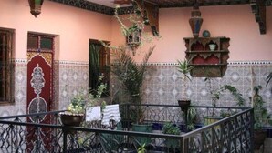 A courtyard with a tiled wall, hanging plants, and a traditional Moroccan-style door. - Hotel Aday (Marrakech)