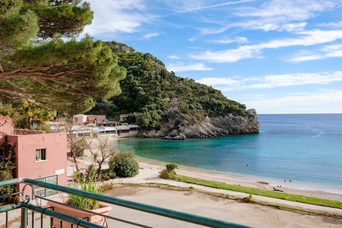 A coastal view with a beach, a rocky hill, and a building with a balcony.
