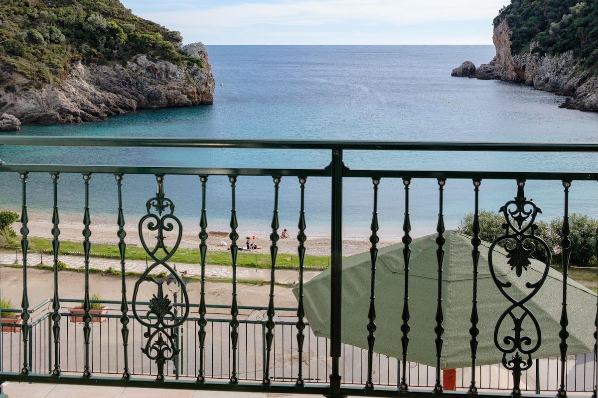 A balcony with a view of a coastal landscape, including a clear sky and calm sea.