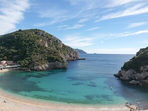 Paisagem costeira com vista clara para o mar, falésias rochosas e uma praia.