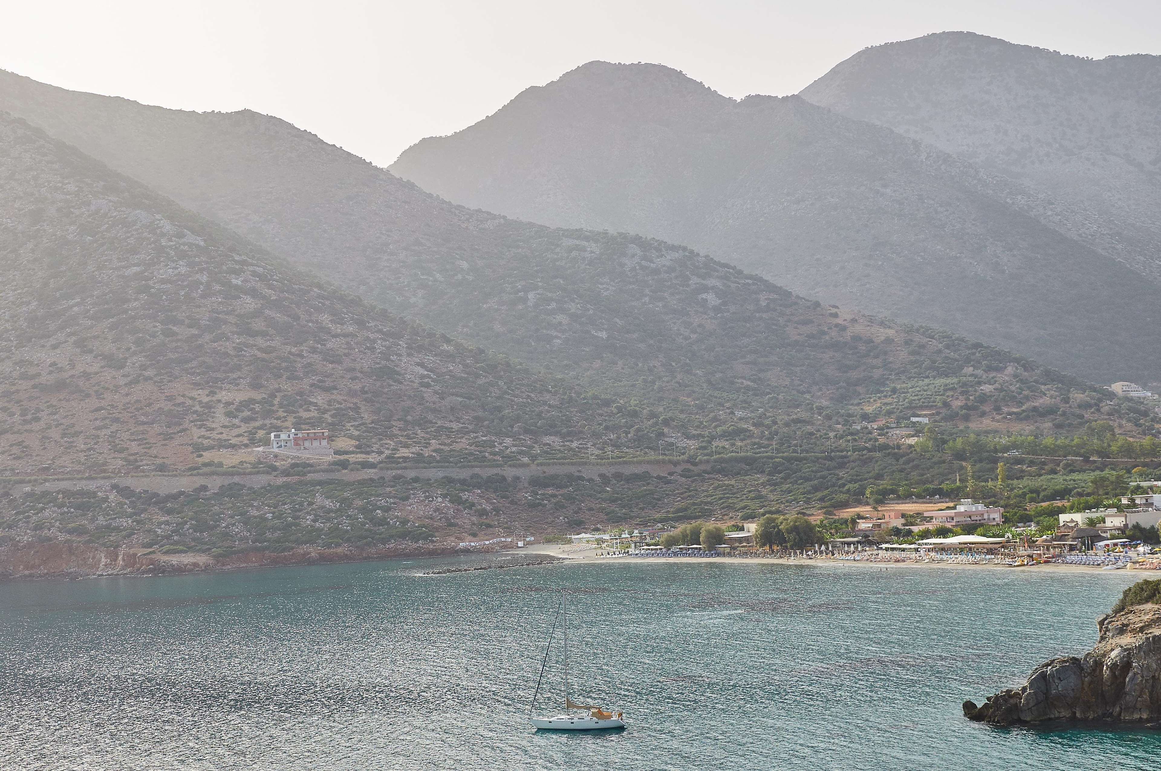 A coastal scene with a boat on calm waters, a beach, and a mountainous backdrop.