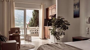 Habitación de hotel con cama, una mesita con libros, una planta en maceta y vistas a un balcón con silla y mesa.