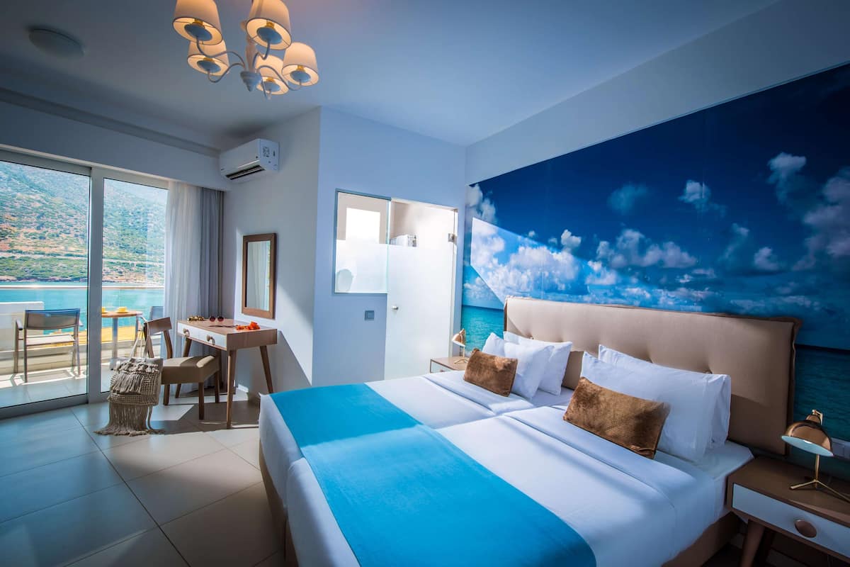 A hotel room with a large bed, a desk, and a view of the sea.