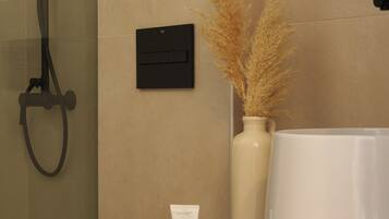 A bathroom with a glass shower enclosure, a white toilet, a vanity with a mirror, and toiletries on the counter.