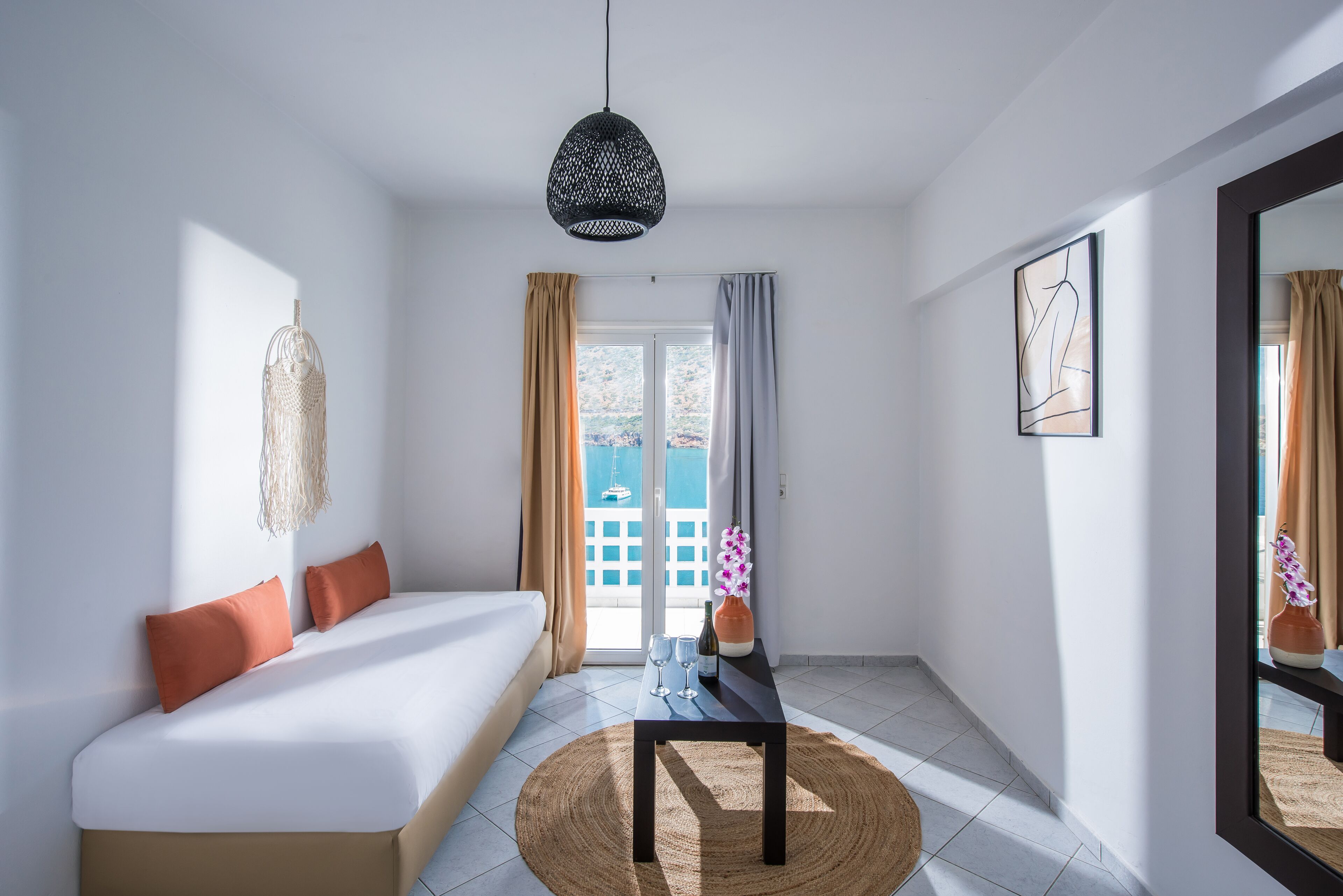 Una habitación de hotel moderna con una cama, una mesita con vasos y una botella, un tapete tejido y un espejo grande.