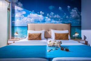 Habitación de hotel con una cama grande, dos mesitas de noche, vista al océano y una escena de playa en la pared.