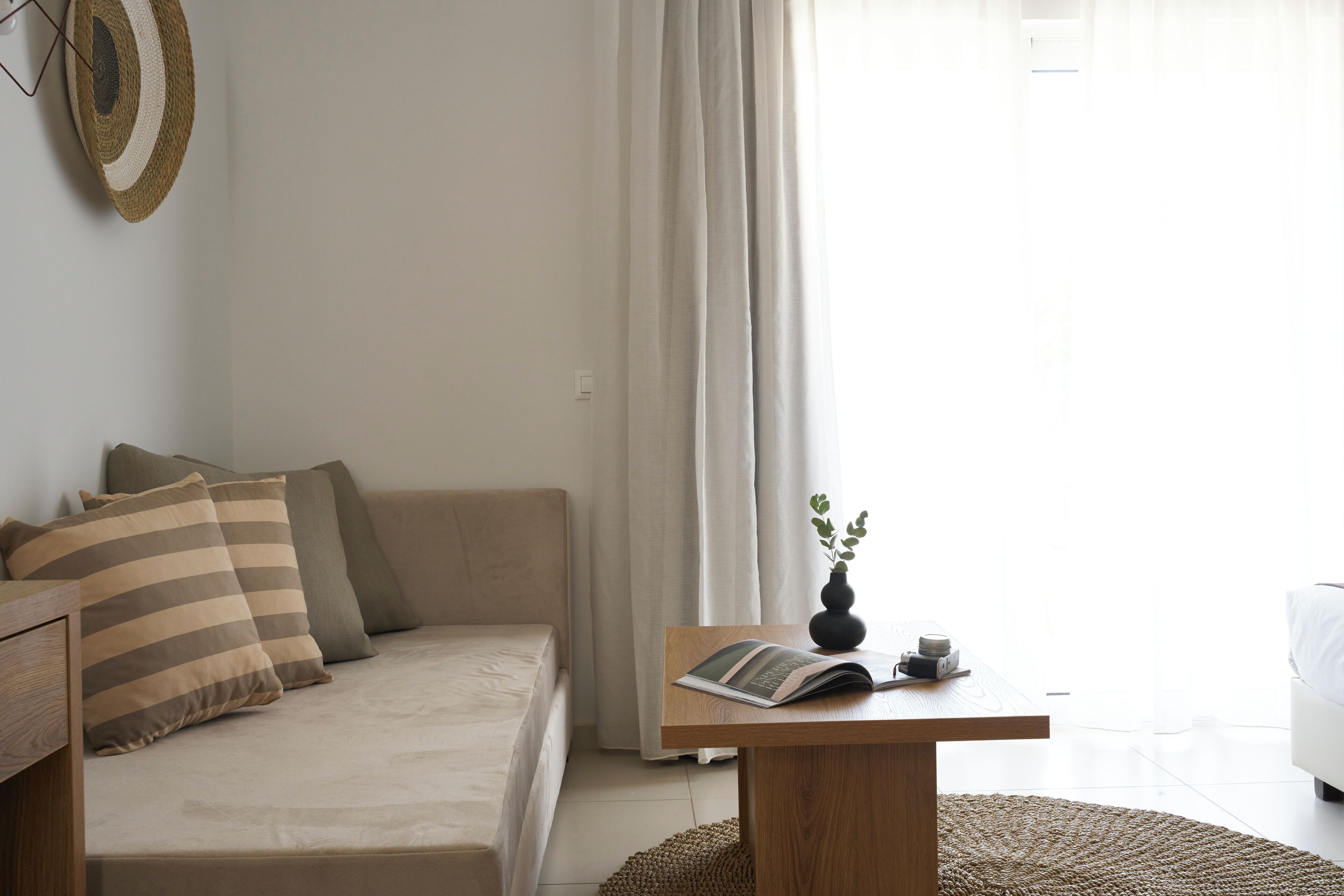 A modern living room with a sofa, a coffee table, and a view through sheer curtains.
