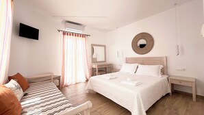 A hotel room with a bed, a bedside table, a chair, a TV, a mirror, and a window with curtains. - Cyclades Blue (Mykonos)