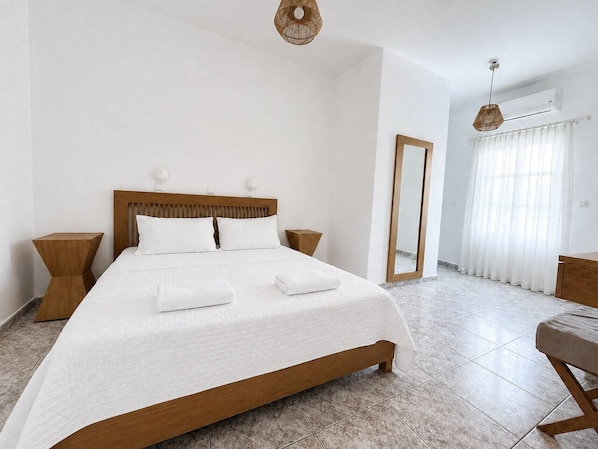 Une chambre d’hôtel avec un grand lit, une tête de lit en bois, deux tables de chevet, un miroir et une fenêtre avec des rideaux.
