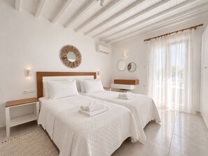 Une chambre d’hôtel avec deux lits, une tête de lit en bois, un miroir rond et une fenêtre avec des rideaux légers.