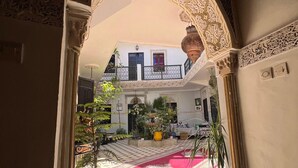 An interior courtyard with a checkered floor, potted plants, and a red patterned rug. - Riad el Farah Kasbah (Marrakech)