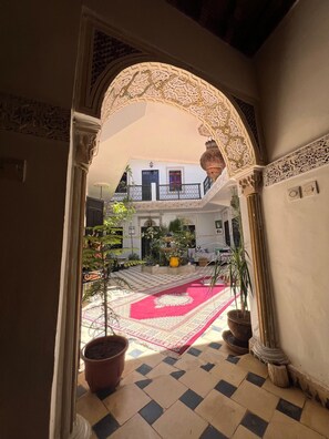 An interior courtyard with a checkered floor, potted plants, and a red patterned rug. - Riad el Farah Kasbah (Marrakech)