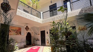 A courtyard with a checkered floor, potted plants, a red carpet, and a balcony with ornate railings. - Riad el Farah Kasbah (Marrakech)