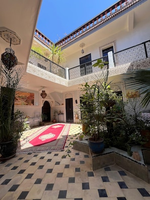 A courtyard with a checkered floor, potted plants, a red carpet, and a balcony with ornate railings. - Riad el Farah Kasbah (Marrakech)