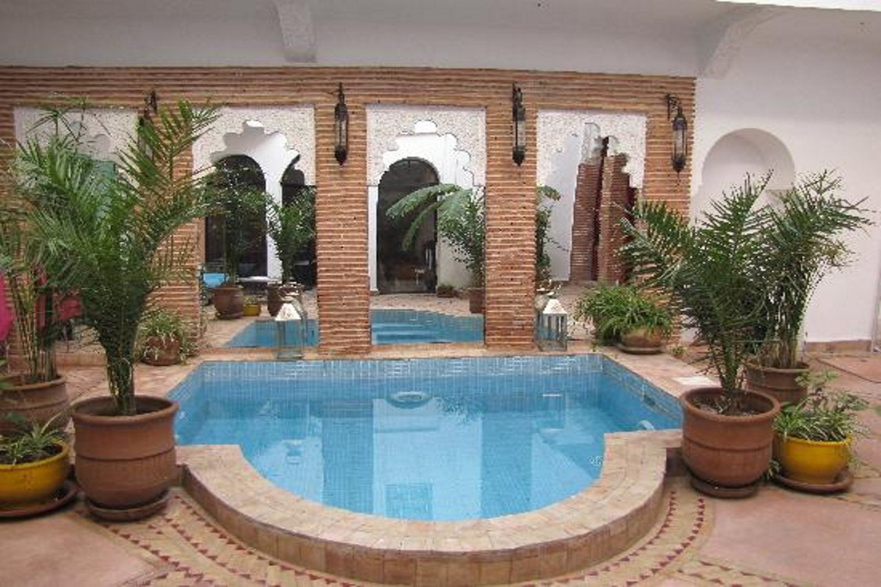 A pool area with a brick wall, arches, and potted plants.