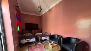 A room with two beds, a round table with a plant, two black leather chairs, a patterned rug, and a hanging light fixture. - Riad el Farah Kasbah (Marrakech)