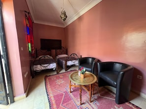 A room with two beds, a round table with a plant, two black leather chairs, a patterned rug, and a hanging light fixture. - Riad el Farah Kasbah (Marrakech)
