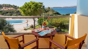 Un balcón con dos sillas de madera, una mesa con un jarrón de flores y vistas a una piscina y al paisaje.