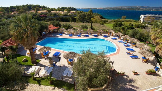 Zona de piscina hotelera con sillones y sombrillas, rodeada de vegetación y vistas al mar.