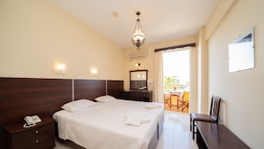 Una habitación de hotel con una cama grande, una mesita de noche de madera con un teléfono, un escritorio con una silla, una lámpara de araña y un balcón con una mesa y sillas.