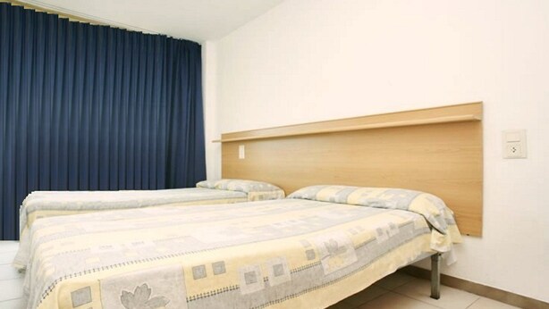 A hotel room with two beds, a wooden headboard, and a blue curtain. - Catalonia Park Apartments (Salou)