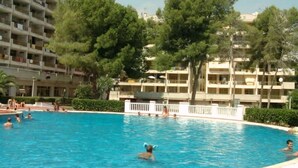 A swimming pool surrounded by multi-story buildings, trees, and a clear sky. - Catalonia Park Apartments (Salou)