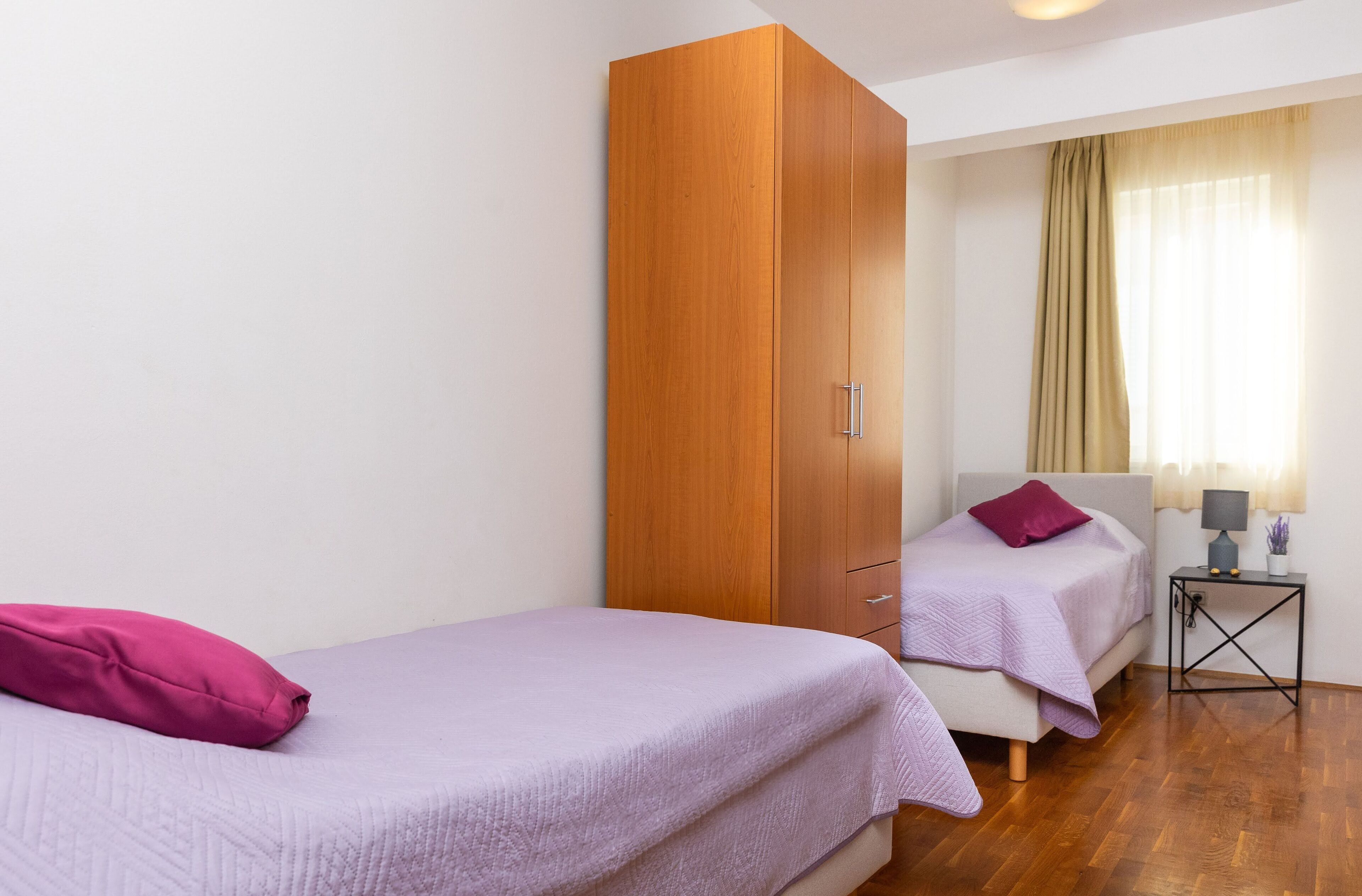 Une chambre avec un lit simple, une armoire, une table de chevet et une fenêtre avec des rideaux.