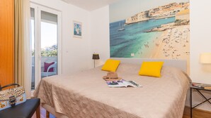 A bedroom with a bed, a view of a beach, a door, and a chair. - Villa Erna (Dubrovnik)